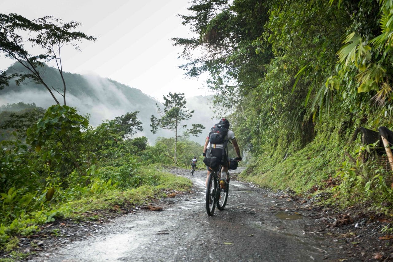 Loaded bikepacking bike on a steep gravel road in the Colombian Andes, misty cloud forest in the background